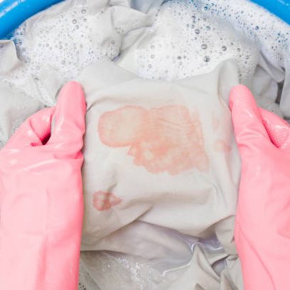 istockphoto-1293598239-612x612 Hands in rubber protective gloves washing sheet with blood stain in blue basin. Point of view shot. Closeup. Top down view.